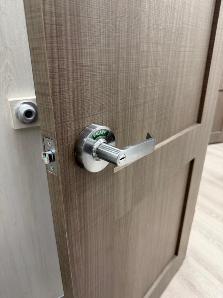 Satin chrome commercial privacy lever with a green VACANT indicator installed on an office restroom door in Edmond, OK