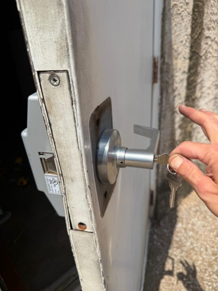 Locksmith testing a freshly cut key in a commercial lever lock on a steel door with an exit device
