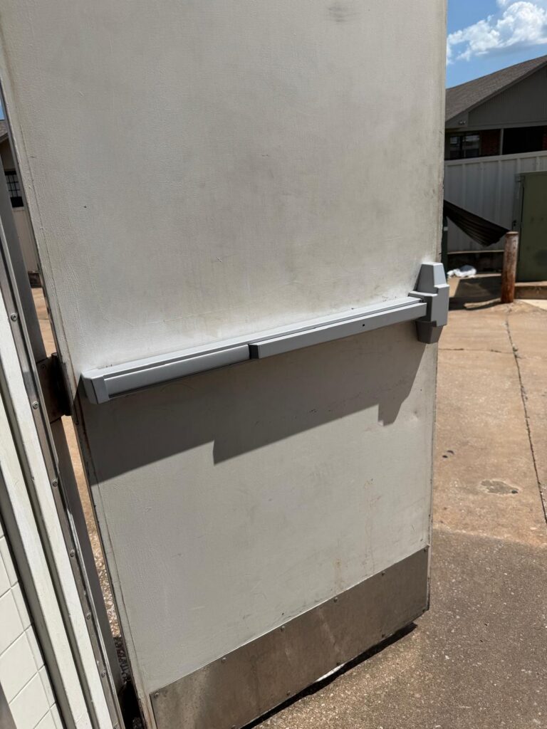 Grey commercial panic bar exit device installed on a steel back door in Oklahoma City
