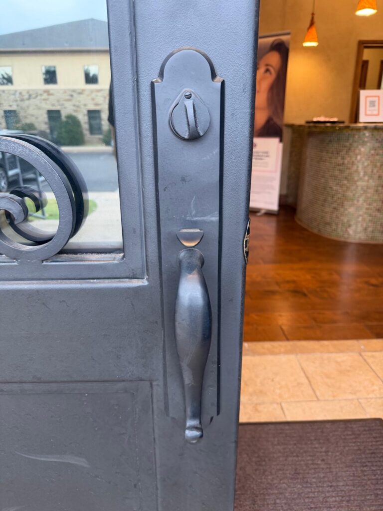 Black wrought iron storefront door with a matching handleset and deadbolt thumbturn at an Edmond, OK business